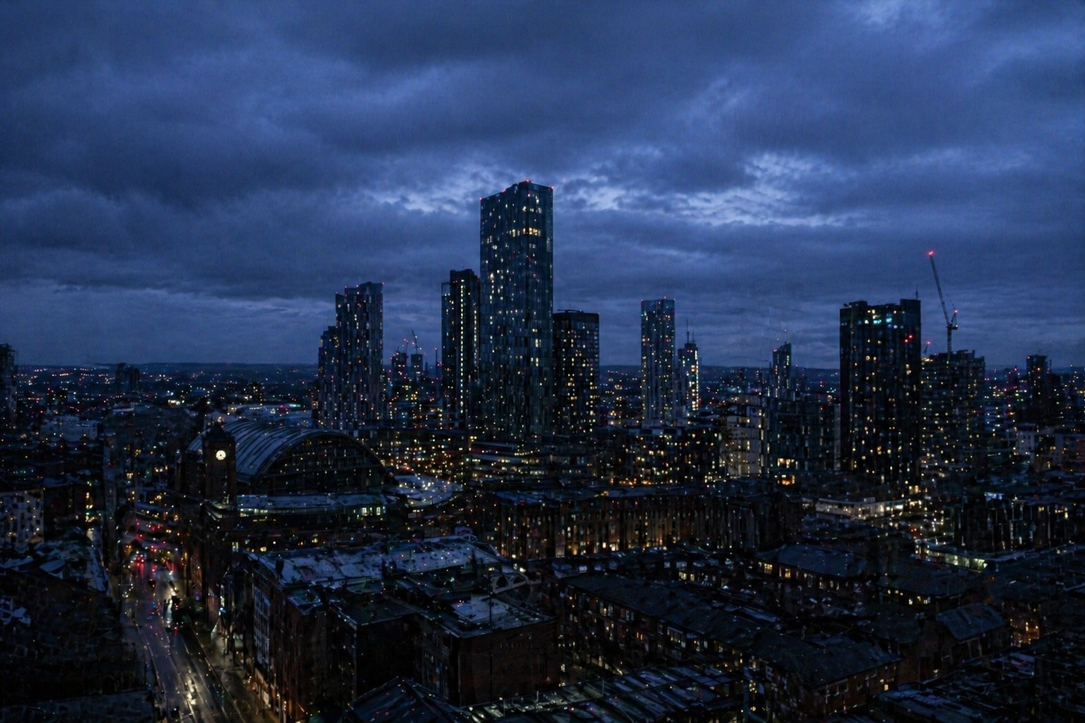 Cinematic deep blue Manchester skyline at night with glowing city lights under moody clouds
